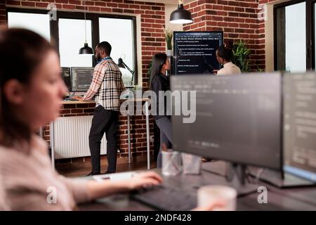 Diverse tech enginners analyzing machine learning app code on programming big screen, standing in it company office. Software developers working on database system with html script. Coding concept Stock Photo
