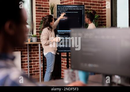 Team of coders talking about algorithms in front of big screen, analyzing html script language. Software developers discussing database on terminal window working in it programming agency Stock Photo