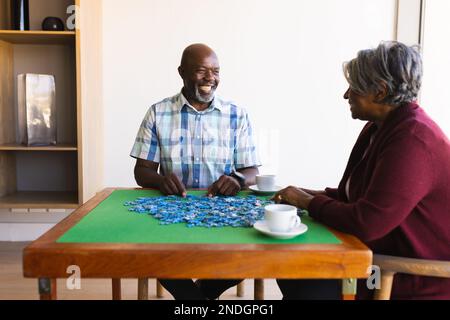 African american senior couple smiling while solving jigsaw puzzle at home. retirement senior lifestyle and living concept Stock Photo