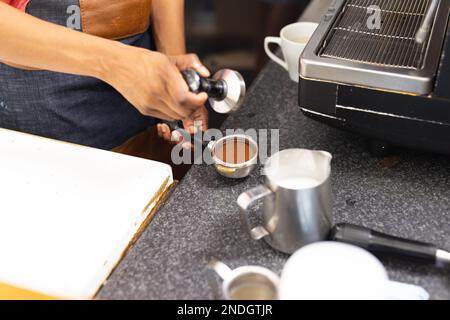 Biracial female barista wearing apron and preparing coffee in cafe. Cafe, free time and city concept. Stock Photo
