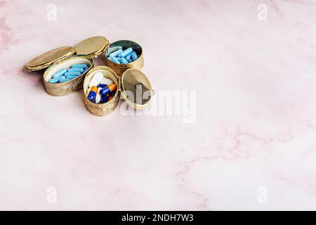 Various golden metal hinged lid pillboxes filled with pills and capsules on a pink marble surface Stock Photo