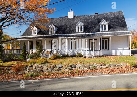 Old renovated 1650s Manoir Gourdeau house facade with white roughcast finish and steel blue trim in autumn, Quebec, Canada. This image is property rel Stock Photo