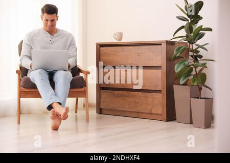 Man with laptop sitting in armchair at home. Floor heating system Stock Photo