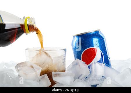 MYKOLAIV, UKRAINE - FEBRUARY 11, 2021: Pouring Pepsi from plastic bottle into glass on ice cubes against white background, closeup Stock Photo