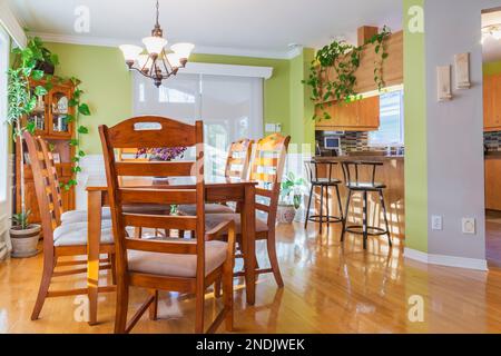 Ash wood table and chairs in dining room with oak wood floorboards, buffet and kitchen counter with bar stools inside country style home. Stock Photo