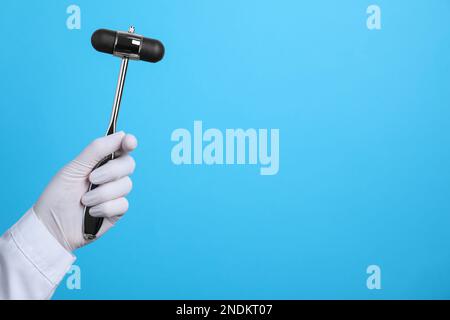Doctor holding reflex hammer on light blue background, closeup with space for text. Nervous system diagnostic Stock Photo