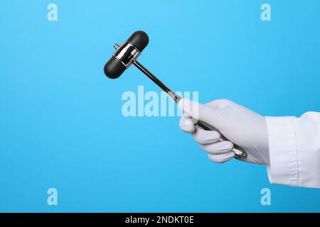 Doctor holding reflex hammer on light blue background, closeup. Nervous system diagnostic Stock Photo