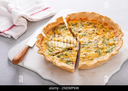 Homemade quiche with ham, cheddar cheese and parsley cut on the table Stock Photo