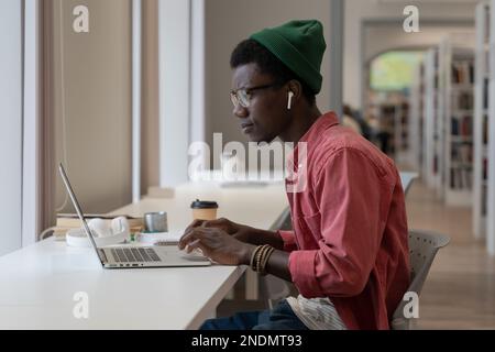 Pondered black intern man employee look at laptop screen typing text or browsing web for education. Stock Photo