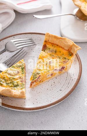 Homemade quiche with ham, cheddar cheese and parsley cut on the table with slices on a plate Stock Photo