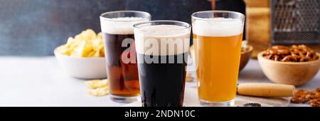 Variety of beer with dark stout, traditional lager and belgian white served with snacks on the table banner Stock Photo