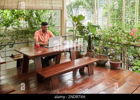 Serious Indian developer sitting at cafe table and working on laptop Stock Photo