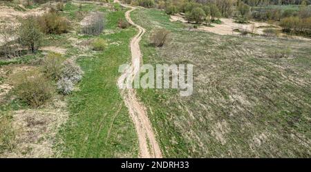 countryside landscape with dirt winding road among green field at early spring. aerial view. Stock Photo