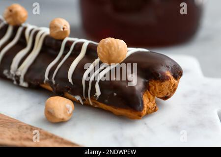 Board with delicious chocolate eclair and hazelnuts on grey table Stock Photo