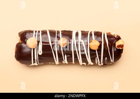 Delicious chocolate eclair with hazelnuts on beige background Stock Photo