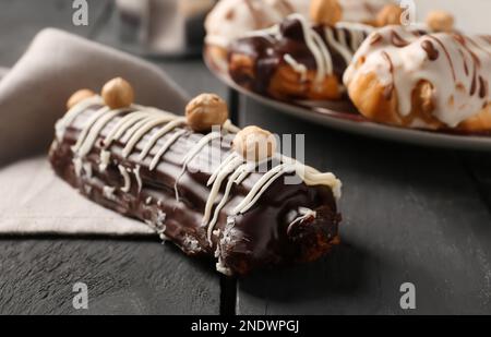 Delicious chocolate eclair with hazelnuts on black wooden table, closeup Stock Photo