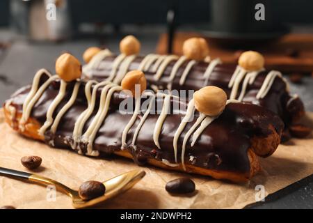 Parchment with delicious chocolate eclairs, hazelnuts and coffee beans on black wooden table Stock Photo