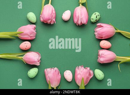 Frame made of beautiful tulip flowers and Easter eggs on green background Stock Photo