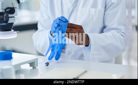 Safety first. Closeup of an unrecognizable scientist putting protective gloves on while doing experiments inside of a laboratory. Stock Photo