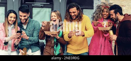 A group of millennials of various ethnicities eat takeout and drink beer under city porticos on a weekend afternoon. They are casually dressed and soc Stock Photo