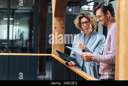 business people analysing a financial report together. Two business people discussing in an office. Happy professionals looking pleased with the succe Stock Photo
