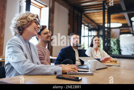 Conference meeting in an office, happy business team sits together in a boardroom discussing work. Team of business professionals collaborating on a p Stock Photo