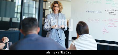 business woman standing in front her team discussing her ideas. business team having a meeting in a boardroom. Creative business professionals working Stock Photo