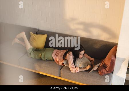 Non-binary trans woman using digital tablet lying on the couch at home. concept of gender fluidity Stock Photo