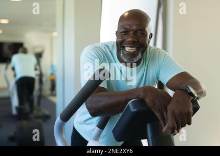 Portrait of african american senior man smiling while standing on elliptical machine at the gym. retirement senior lifestyle and living concept Stock Photo