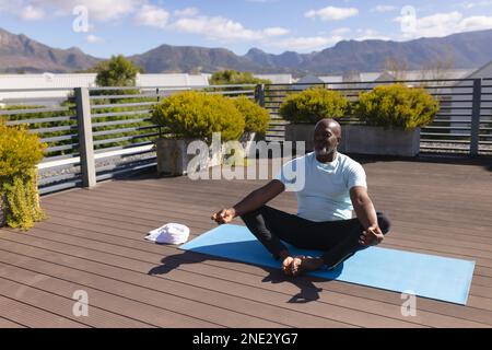 African american senior man practicing yoga and meditating on the terrace at home. retirement senior lifestyle and living concept Stock Photo
