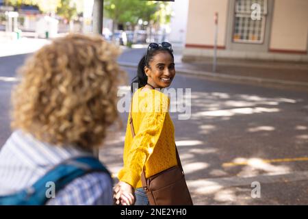 Happy diverse couple wearing sunglasses and holding hands in city. On the go, travel and city concept. Stock Photo