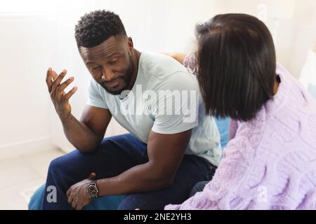 Sad diverse couple sitting on bed and embracing. Spending quality time at home, domestic life and lifestyle concept. Stock Photo