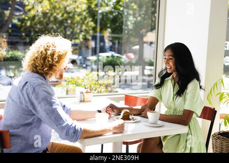 Happy diverse couple sitting at table and talking with cup of coffee in cafe. Cafe, free time and city concept. Stock Photo
