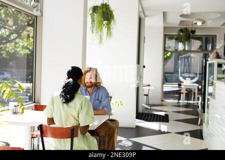 Happy diverse couple sitting at table and talking in cafe. Cafe, free time and city concept. Stock Photo