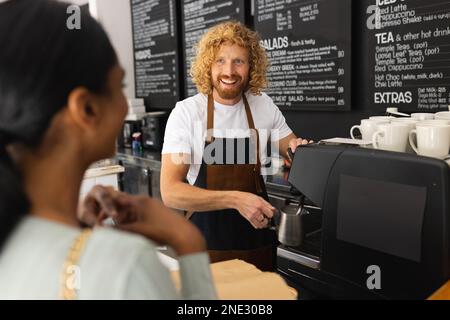 Happy diverse woman and male barista preparing coffee in cafe. Cafe, free time and city concept. Stock Photo