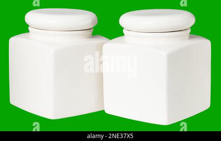 two white ceramic jars for food storage in the kitchen isolate on a green background. Stock Photo