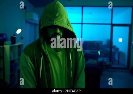 Man, hacking or dark hoodie in neon living room with cybersecurity, software programming or phishing mystery. Hacker, hood or night clothes with Stock Photo