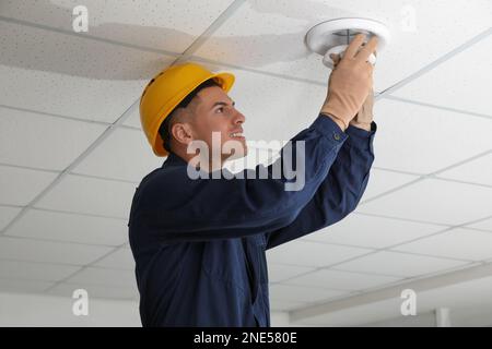 Electrician in uniform repairing ceiling lamp indoors Stock Photo