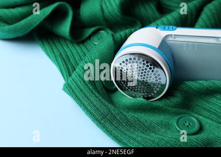 Modern fabric shaver and woolen cardigan on light blue background, closeup Stock Photo