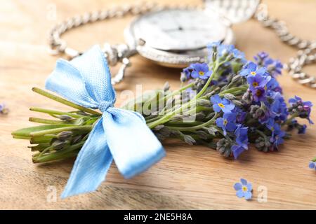 Beautiful blue forget-me-not flowers tied with ribbon on wooden table, closeup Stock Photo