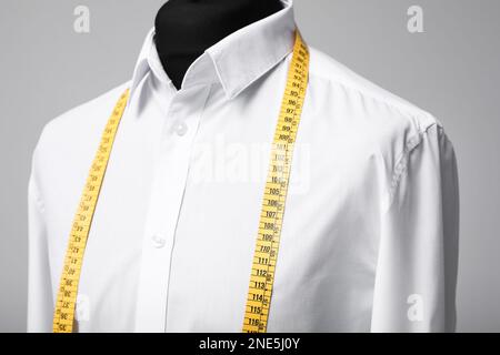 White shirt with tailor's measuring tape on mannequin against grey background, closeup Stock Photo