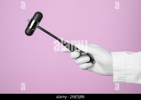 Doctor holding reflex hammer on pink background, closeup. Nervous system diagnostic Stock Photo