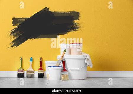 Set with decorator's tools and paint on floor near yellow wall Stock Photo