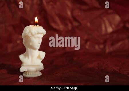 Beautiful burning David bust candle on red crumpled parchment. Space for text Stock Photo