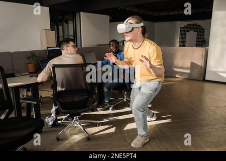 IT Development Team Working on VR Project. Man wearing VR headset, playing and touching something in the virtual world. Diverse men programmers using Stock Photo
