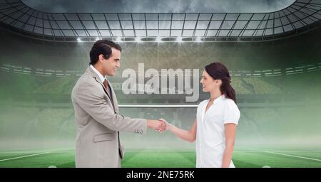 Composition of businessman and businesswoman shaking hands over sports stadium Stock Photo