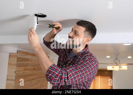Man with screwdriver repairing ceiling lamp indoors Stock Photo