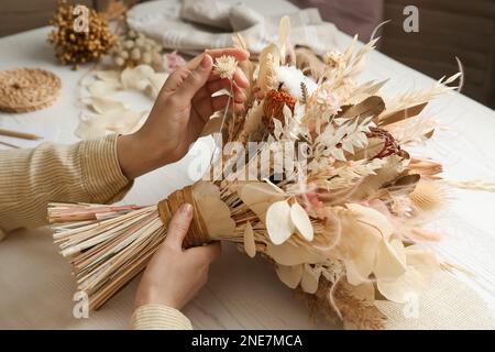 Florist making beautiful bouquet of dried flowers at white table, closeup Stock Photo