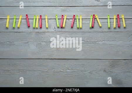 Colorful plastic clothespins and rope on grey wooden background. Space for text Stock Photo