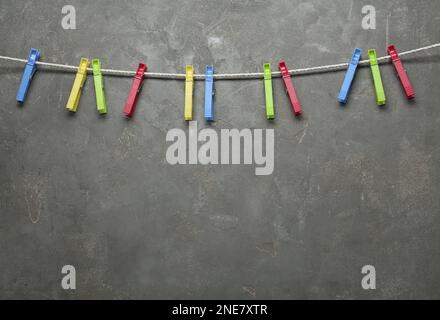 Colorful plastic clothespins and rope on grey stone background. Space for text Stock Photo
